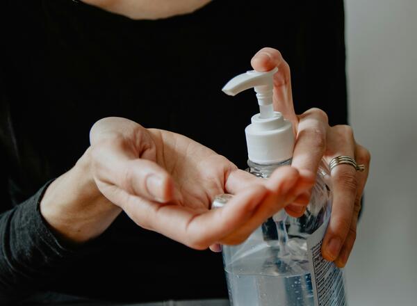 Hands of person holding bottle of hand sanitizer in one hand and pumping into other hand