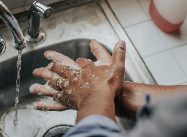 Hands of person of color washing at sink