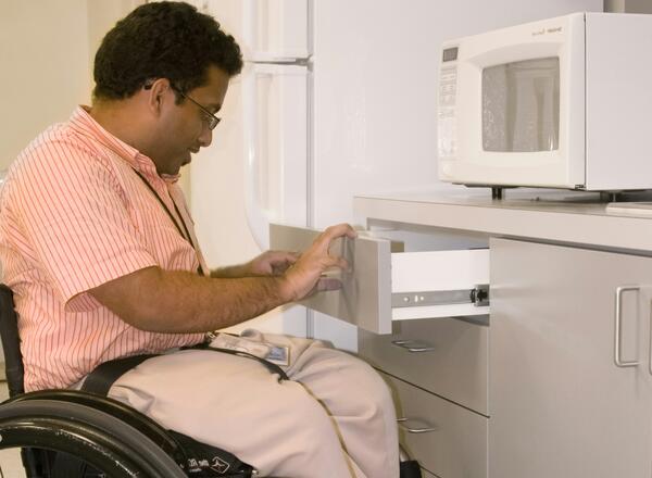 Person in wheelchair opening cabinet drawer near microwave