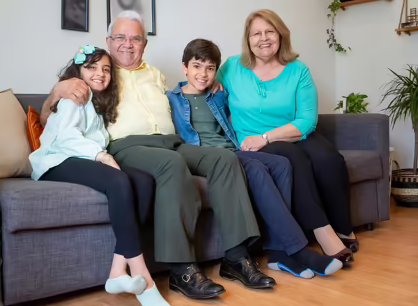 An elderly couple smile with two young children while they sit on a couch.