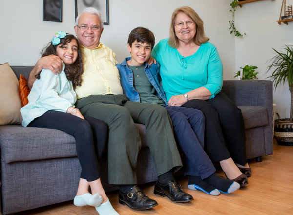 An elderly couple smile with two young children while they sit on a couch.