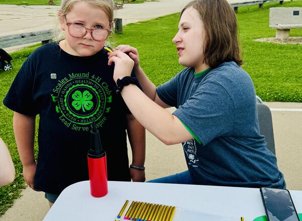 Maci Burbach holds still while 4-H Federation member Faith Morhardt, Elizabeth, paints a design on her face during the Cloverbud Round-Up.