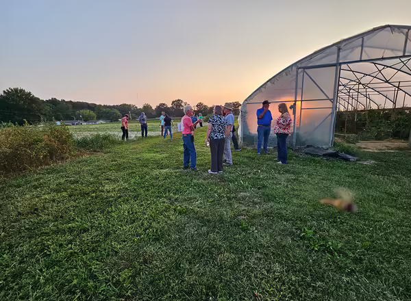 group of people standing beside a high tunnel in a field