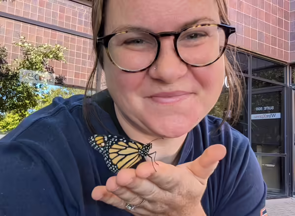 woman with glasses holding a monarch butterfly on hand