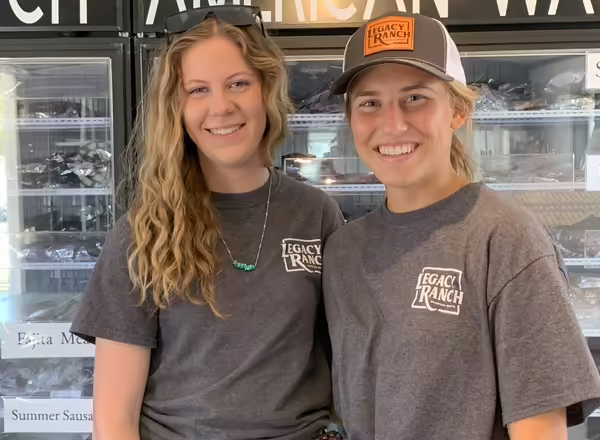 Kylie Balducci and Naomi Wegner in gray t-shirts in front of a meat cooler
