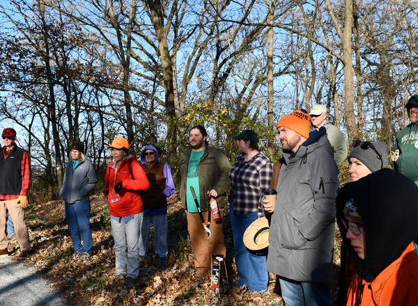 A group listens to a speaker in the woods.