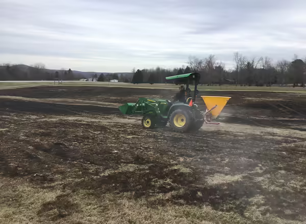 tractor spreading seed mix on DSAC pollinator prairie after a controlled burn