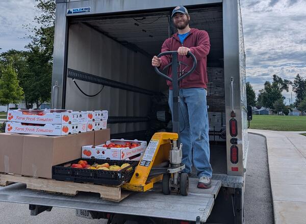 a man stands with a pallet of tomatoes on a truck 