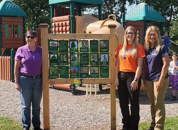 three woman stand next two a new sign at a children's park