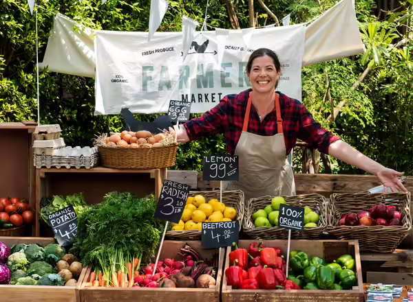 a female farmers market vendor stands with colorful produce