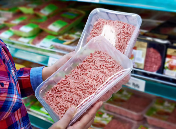 person at supermarket holding two packages of ground meat