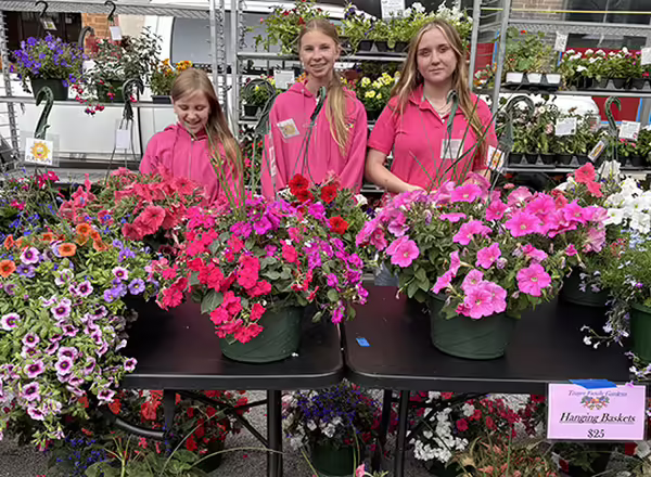 3 of Cathy's grandchildren at their market booth displaying flower baskets