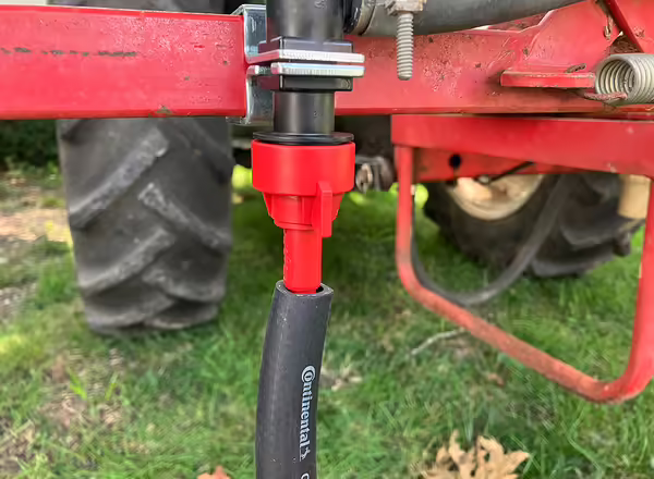 red plastic nozzle on a fitting on back of tractor with a black hose attached to the bottom