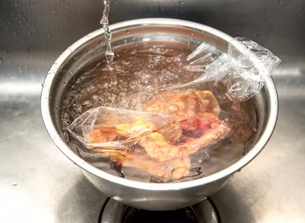 frozen chicken in sealed plastic bag submerged in bowl of water