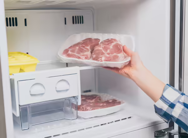 A person taking a package of frozen meat out of a freezer.