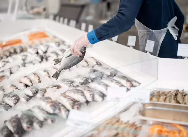 A person choosing fish from a glass seafood case.