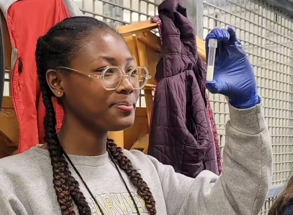 Young woman wears blue laboratory gloves and holds up a test tube to eye level