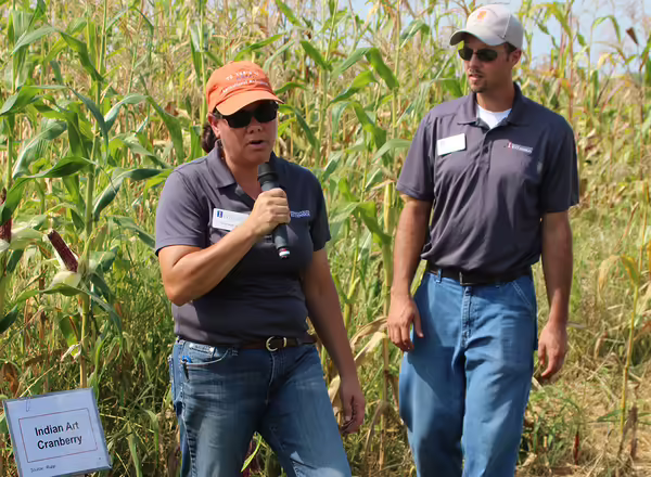 two people standing in a corn field with a microphone