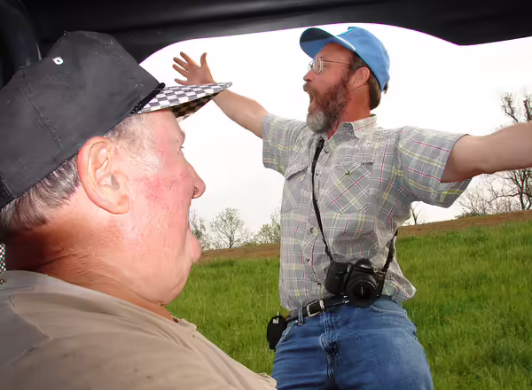 person wearing a hat in a vehicle and a person wearing a hat talking in a field