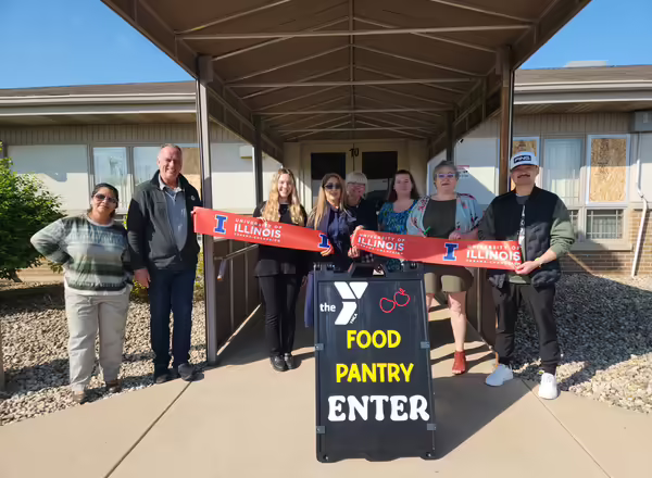 A group of community leaders during a food pantry grand opening pose with a cut ribbon. A sign in front of them reads "Food Pantry Enter"