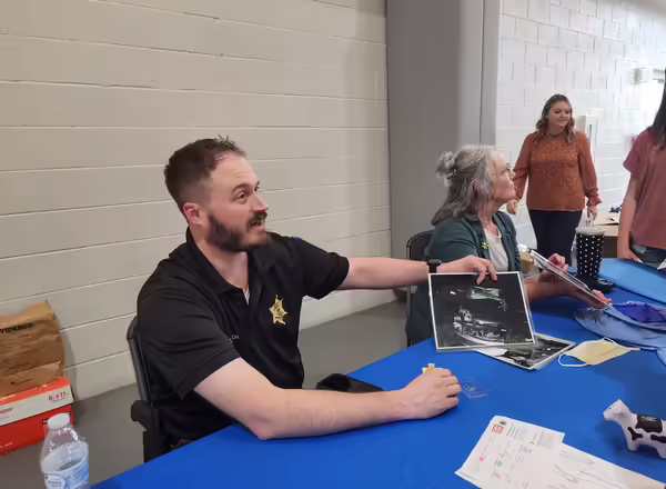 Two people sit at a table showing pictures to a group of students