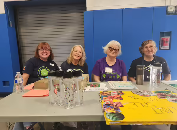 Four master gardener volunteers are seated at a table at the plant sale
