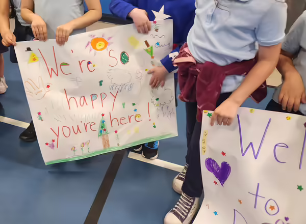 Students hold handmade signs that read "We're so happy you're here!"