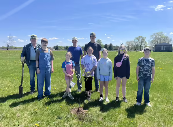 4-H youth and partners pose beside a newly planted tree.