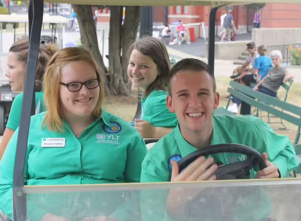 Kevin drives a golf cart with three other youth leadership team members. They are all wearing green dress shirts