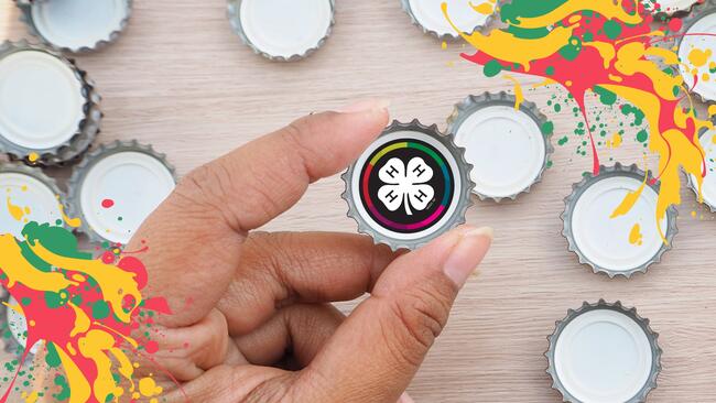 hand holding a bottle cap with a 4-H clover on it