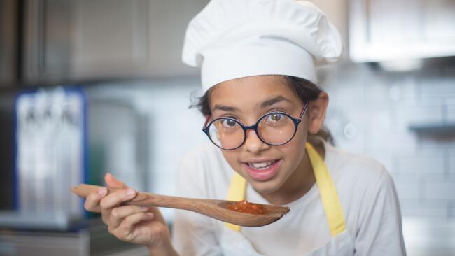A girl wearing a chefs hat and holding a spoon 