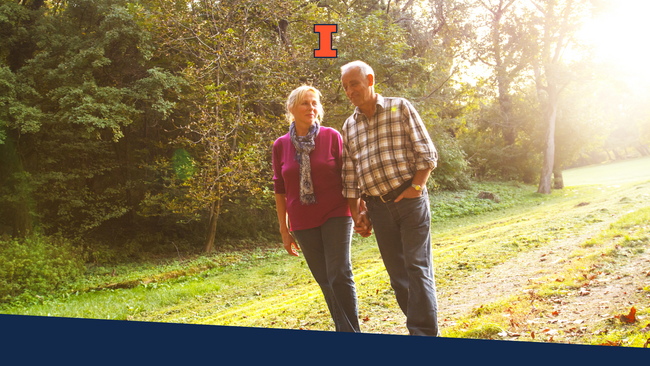 A senior couple walking along a path with trees behind them.