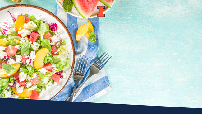 Summer watermelon salad with leaves of lettuce, watermelon, peaches, and feta sitting on a light blue background.