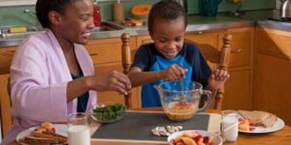 Woman and child at kitchen table putting ingredients into a mixing bowl
