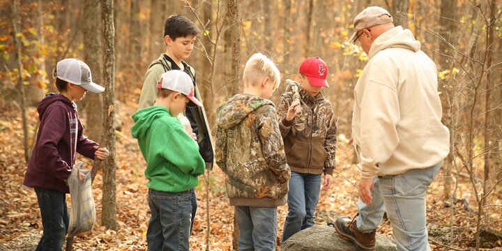 4-Hers observe a large rock in the woods looking for fossils