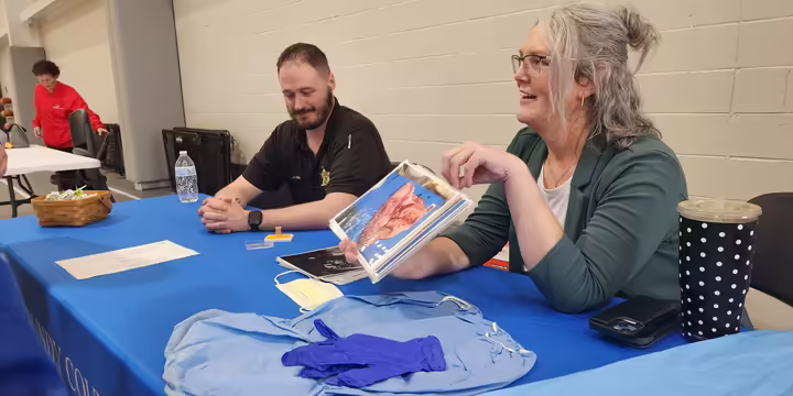 Two people sit at a table, showing images to a group of students