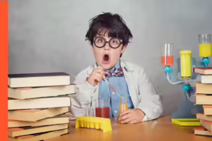 behind the desk is a kid scientist with crazy hair dropping chemicals into a flask. on the desk is a beaker and books.