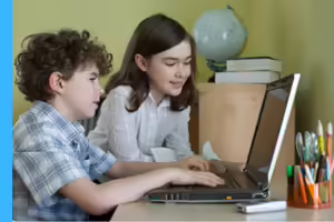 a boy working on a laptop with a girl watching