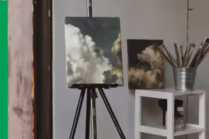 canvas on a easel with a stand next to it with a bucket of paint brushes