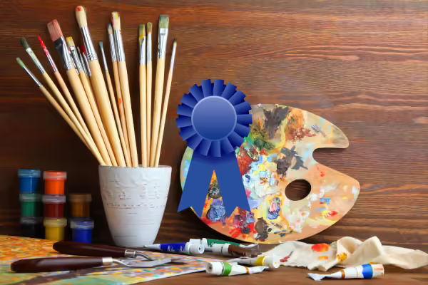 Art supplies on a table with a graphic of a blue ribbon over the top of the image.