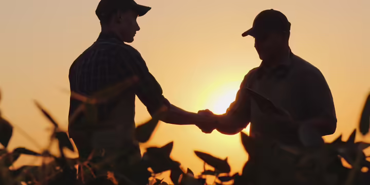 two men shaking hands in a farm field