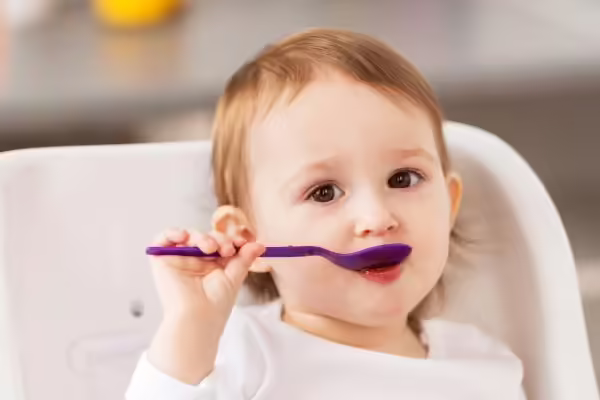 Baby girl using spoon to eat puree