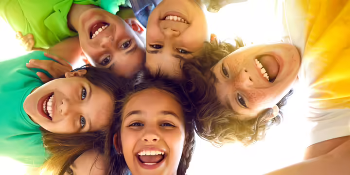 Group portrait of happy kids huddling, looking down at camera and smiling