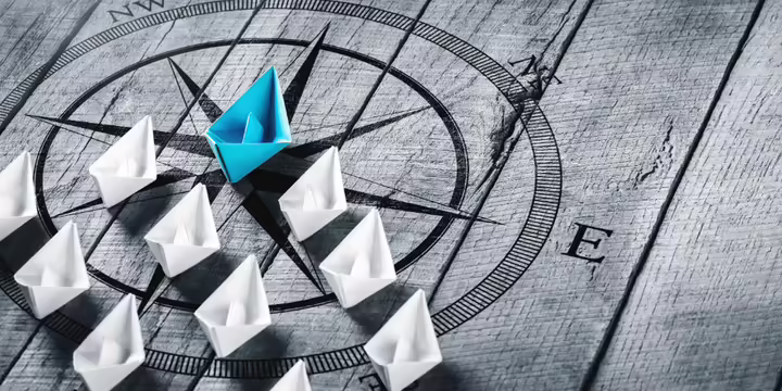 blue paper boat followed by many white paper boats