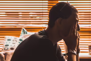 Man sitting on couch while holding hands in front of face