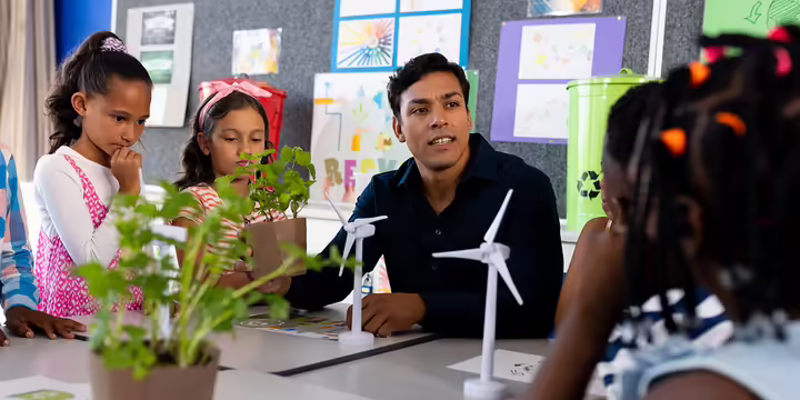 a teacher in a classroom with students, plants and models of wind turbines