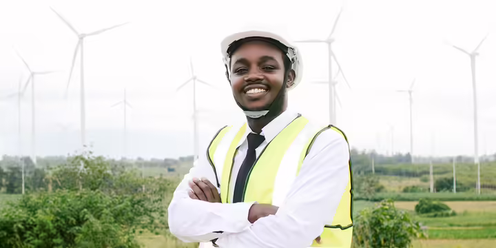 a man with a hard had stands in front of wind turbines