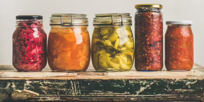 Five glass jars of preserved foods arranged on a rustic wooden table.