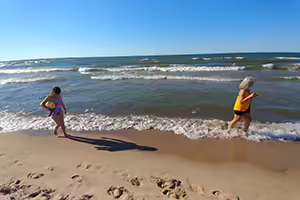 Child carrying beachball walking behind adult on Lake Michigan shore