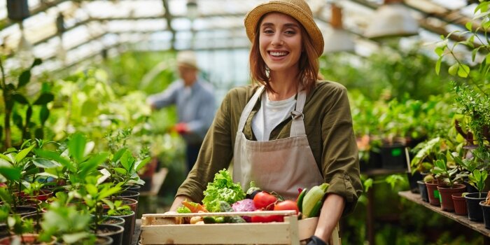 woman in greenhouse with a crate of vegetables